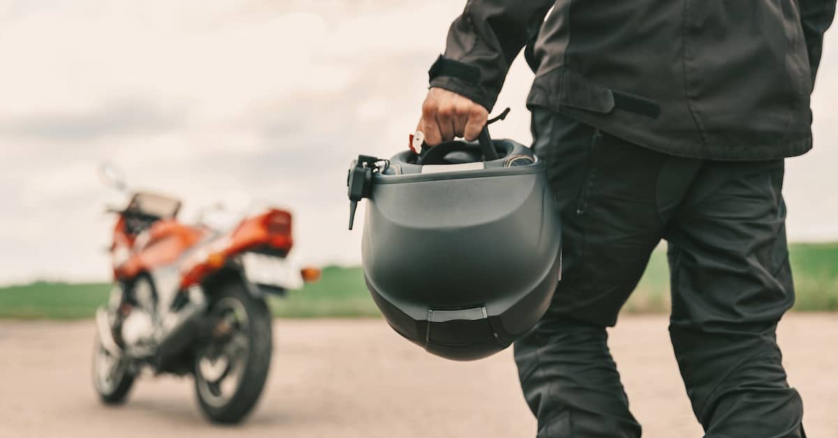 Motorcyclist carrying a motorcycle helmet walking toward his motorcycle | The Haynes Firm