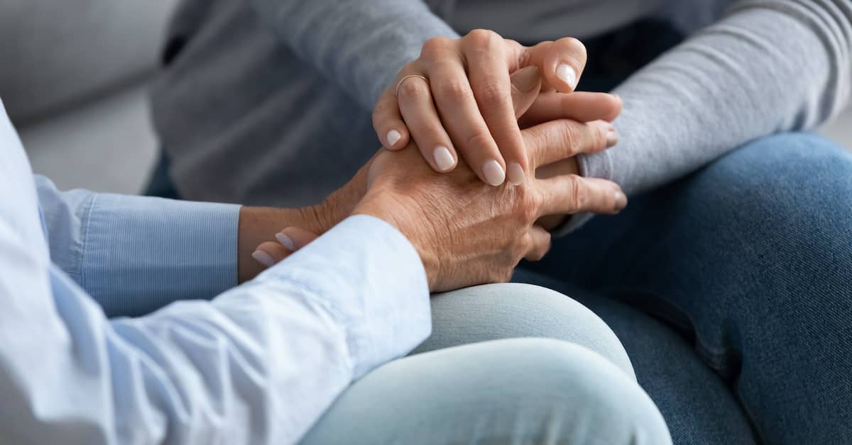 young woman holding the hands of a grieving older woman